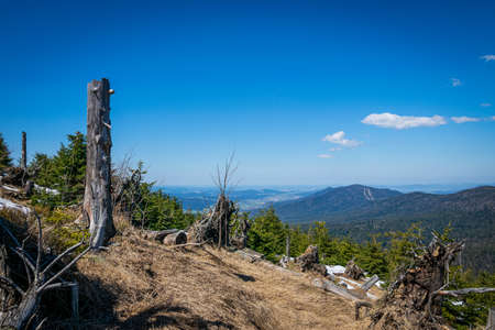 View from the top of a mountain into the valley with clouds in the blue sky and beautiful green trees and lots of rocksの写真素材