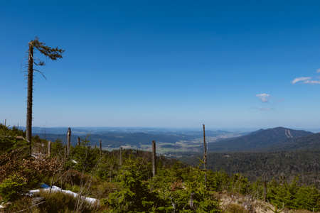 View from the top of a mountain into the valley with clouds in the blue sky and beautiful green trees and lots of rocksの写真素材