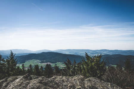 View from the top of a mountain into the valley with clouds in the blue sky and beautiful green trees and lots of rocksの写真素材
