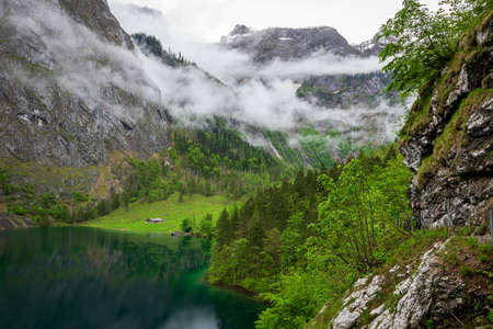 View of the mountains in Berchtesgaden on the Koenigssee with clouds in the sky and stones and rocks in the foregroundの写真素材