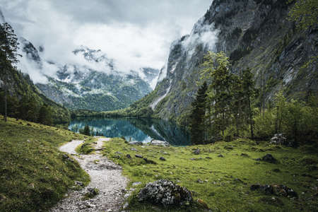 View over the Obersee in bavaria near berchtesgaden with mountains and clouds in the background and reflection on the waterの写真素材