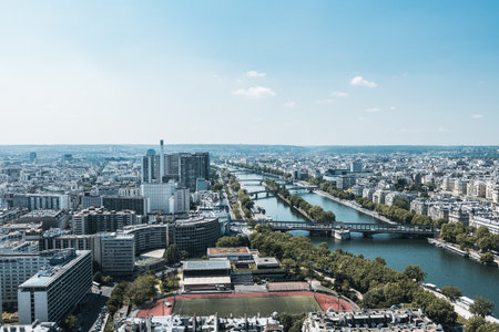 A panoramic aerial view of Paris featuring the Seine River winding through the city, modern buildings, bridges, and urban greenery. The image captures a mix of contemporary and classic Parisian architecture under a bright blue sky. Ideal for travel, cityscape, and architectural themes.の写真素材