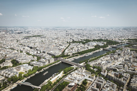 A panoramic aerial view of Paris featuring the Seine River winding through the city, modern buildings, bridges, and urban greenery. The image captures a mix of contemporary and classic Parisian architecture under a bright blue sky. Ideal for travel, cityscape, and architectural themes.の写真素材