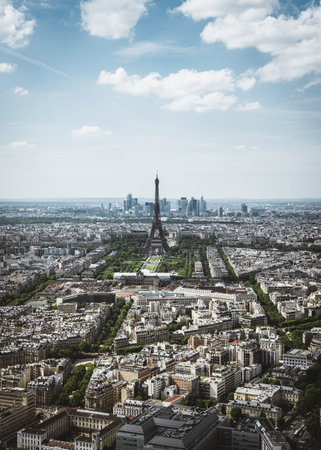 A stunning aerial view of Paris, showcasing the iconic Eiffel Tower surrounded by historic architecture and lush green trees under a dramatic sky with scattered clouds. Captured during daylight, this image highlights the charm and grandeur of the French capital's urban landscape. Perfect for travel, tourism, and architecture themes.の写真素材