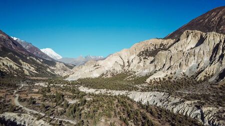 A harsh mountains slopes on the way to Humde, Annapurna Circus Trek, Himalayas, Nepal. Captured with a drone, from above.Beautiful clear blue sky. in the back white mountain peaks visible.の写真素材