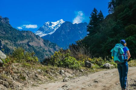 Trekking girl with a big blue backpack admires Manaslu, Annapurna Circuit Trek, Nepal. Forest to the...