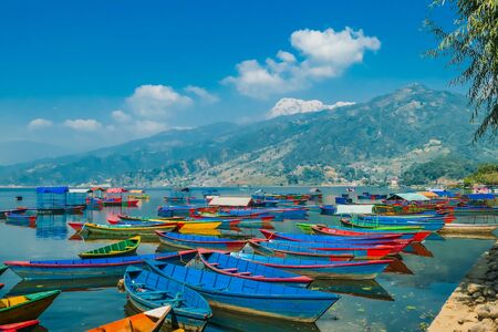 Many colourful boats parked on the shore of Phewa lake, Pokhara, Nepal. In the back Himalayan mountain range. Small villages visible on the shore. Peaceful and chilled atmosphere. Place to relax.の写真素材