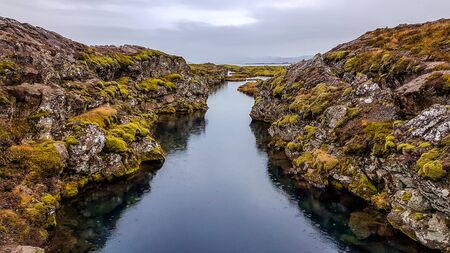 Ãingvellir National Park in Iceland, a place where two tectonic plates meet underwater, the Eurasian tectonic plate and the North American tectonic plate. A narrow water tunnel surrounded by hills.の写真素材