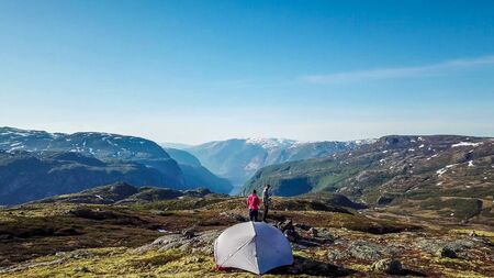 A couple standing at the rock, enjoying the view on Eidfjord, Norway. They are camping in the...
