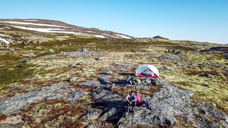 A couple sitting at the rock, enjoying the view on Eidfjord, Norway. They are camping in the...
