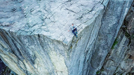 Aerial shot of a young man sitting at the edge of Preikestolen. First morning sunbeams reach the...
