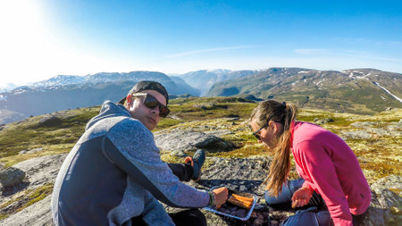 A couple having a grill in the tall mountains. Few sausages are being grilled. Couple uses portable one time grill, picnic grill. Camping in Norwegian wilderness.Clear and bright day.の写真素材