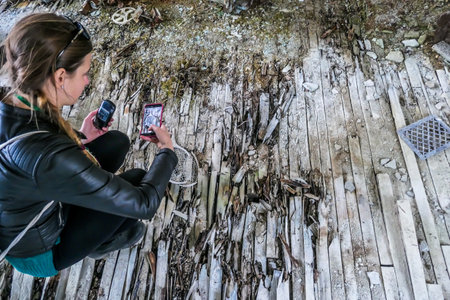 A girl taking a picture of decaying tennis racket decaying on the ground of an abandoned sports hall...