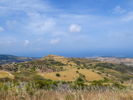 An idyllic view of a hilly fields in Cyprus. Slopes are overgrown with grains and small bushes. In the back some smaller mountains are visible. Great overcast, spreading all over the sky.の写真素材