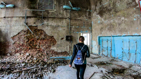 Girl in black outfit walks around the rotten floor in an abandoned sports hall in Pripyat, Ukraine, after the Chernobyl explosion. The floor is completely rotten. Lots of decaying object on the floorの写真素材