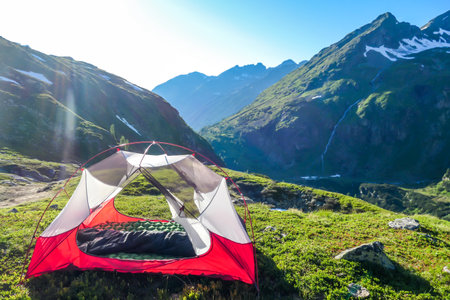 An unfolded tent on a meadow in high Alps. Slopes of the mountains partially covered with snow. Wild camping in Austria. High mountains around. Spring in alpine valleys.の写真素材