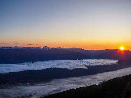 Sunrise over a fog covered snowy Alps in Goldeck, Austria. The sky line is bursting with orange and yellow. There is thick fog in the valley. Soft sunrise colours. Endless mountain chains in the backの写真素材
