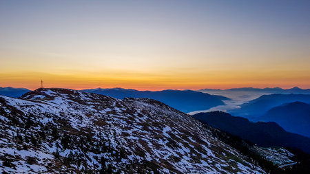 Sunrise over a fog covered snowy Alps in Goldeck, Austria. The sky line is bursting with orange and...