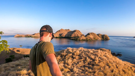 A man walking on top of a small island, enjoying the morning sun over Komodo National Park, Flores,...