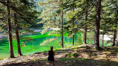 Woman enjoying a peaceful view on Green Lake, located in an Alpine valley in Austria. The algae in the lake give it its distinctive color. Lots of pine trees on the shore. The girl is calm and relaxedの写真素材