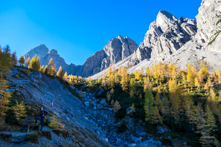 A woman with hiking backpack taking a rest on a bench while hiking to reach the Grosse Gamswiesenspitze in Lienz Dolomites, Austria. Sharp and barren slopes. Massive Alpine mountains. Solo wandererの写真素材