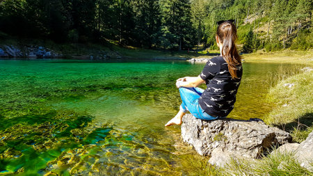 Girl sitting on the stone at the shore of Green Lake in an Alpine valley in Austria and enjoying the...