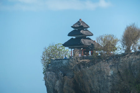 A view on Uluwatu Cliffs, Bali, Indonesia. There is a small temple on the top of the cliff. The waves are rushing to the shore, making the water bubbly. Steep and dangerous fall. Hidden gemの写真素材