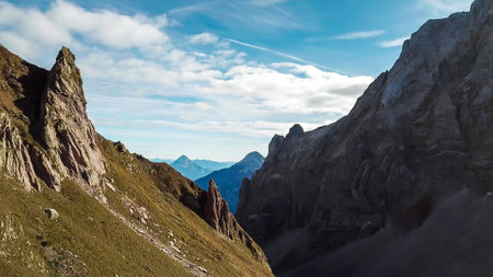 A drone shot of Alpine landscape of Austria. Sharp slopes of both side of the valley. Hard to reach mountain peaks. There are many mountain ranges in the back. Serenity and calmnessの写真素材