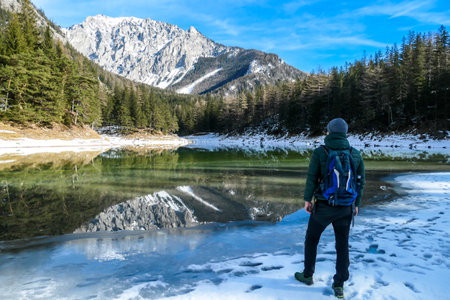 A man walking around the shore of Green Lake, Austria. Powder snow covering the mountains and ground. Soft reflections of Alps in calm lake's water. Winter landscape of Austrian Alps. Calmnessの写真素材
