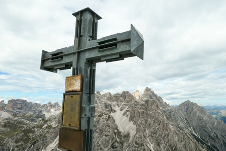 A wooden cross on high and desolated mountain peak in Italian Dolomites. In the back there are endless mountain chains. Raw and unspoiled landscape. Few clouds above the peaks. Sharp and steep slopes.の写真素材