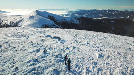 A drone shot of a couple wearing snow shoes hiking up to Amerinkogel's peak in Austrian Alps. Fresh...