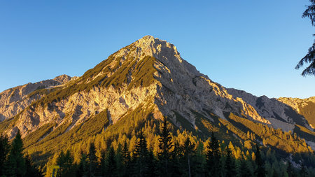 The first sunbeams reaching the top of Mittagskogel in Austrian Alps. The high mountain is overgrown...