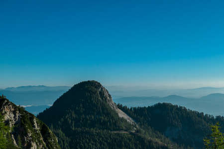 A panoramic view on the Alps from the top of Mittagskogel in Austria. Clear and sunny day. Sharp peaks around. A bit of haze in the valley. Outdoor activity. Alpine mountain chains in the back. Calmの写真素材