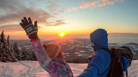 A couple enjoying the sunrise seen from snow-capped peak of Schoeckl in Austrian Alps. The sky is...