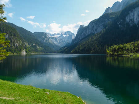 Panoramic view on Gosau lake, with Dachstein glacier in the back in Austrian Alps. The lake is surrounded by high mountains, overgrown with tall trees. Sun reflects on the surface. Serenity  and calmの写真素材