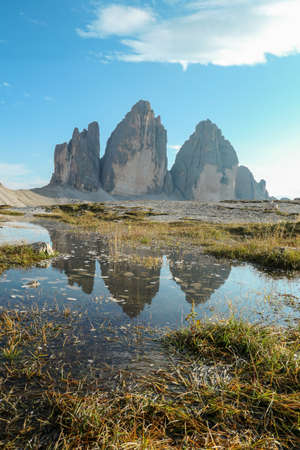 A panoramic view on the famous Tre Cime di Lavaredo (Drei Zinnen), mountains in Italian Dolomites. The mountains are reflecting in small paddle. Desolated and raw landscape. Natural phenomenonの写真素材