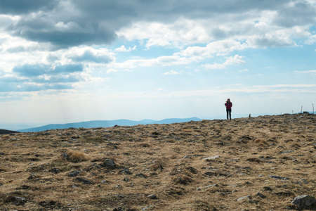 A woman hiking to the top of Ameringkogel in Austrian Alps. The vast pasture is golden. There are other chains in the back. There is no pathway, she is making her own. Achievement and pursuitの写真素材