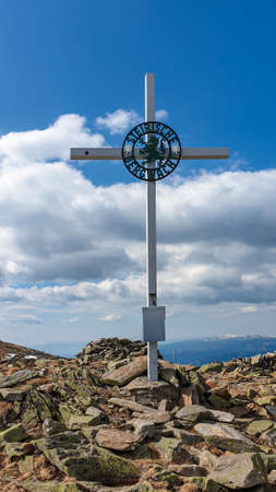 A metal cross on the top of Ameringkogel in Austrian Alps. The cross is surrounded by piles of stones. There are other chains in the back. Blue sky with white clouds on it. Serenity and achievement.の写真素材