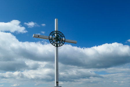 A metal cross on the top of Ameringkogel in Austrian Alps. The cross is surrounded by piles of stones. There are other chains in the back. Blue sky with white clouds on it. Serenity and achievement.の写真素材