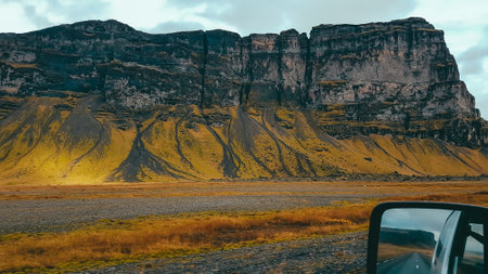 Tall mountains covered with moss, valley consists of lava fields. In the corner a car side mirror, showing the road and another range of mountains. Front and back view. Autumn colors of the plantsの写真素材