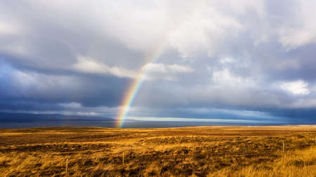A beautiful rainbow stretching across a cloudy sky over a barren grassland. he sky looks as if it just stopped to rain. Beautiful miracle.の写真素材