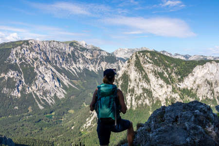 A woman with a hiking backpack admiring the view on the Alpine mountain chains in Austria, Hochschwab region. The slopes are partially overgrown with small bushes, higher parts baren. Happinessの写真素材