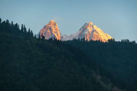 First sunrise reaching the peaks of Ushba in Caucasus, Georgia. Cloudless sky above the high and...