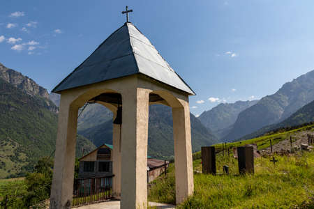 A small bell tower on a lush green pasture in Caucasus, Georgia. There are high mountain chains...
