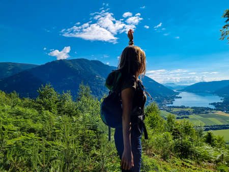 A woman standing at a viewing point near the top of Oswaldiberg with the view on the Lake Ossiach in Austrian Alps, Carinthia. The hiker enjoys a panoramic view on the Ossiacher Tauern. Freedomの写真素材