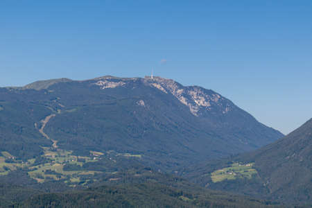 A close up view on Dobratsch, a mountain in Austrian Alps. The mountain's sides are overgrown with lush forest, Peak is baren and sharp. High mountaineering. Clear and blue sky. Calmness.の写真素材