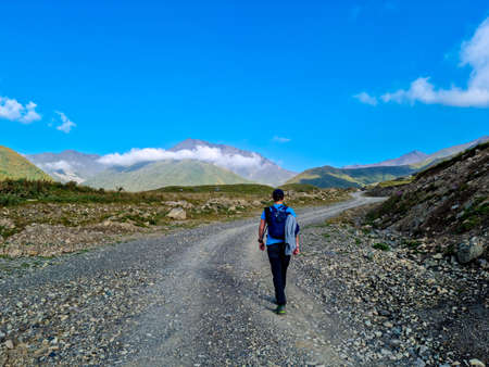 A man walking on a hiking trail with a view on the sharp mountain peaks of the Chaukhi massif in the...