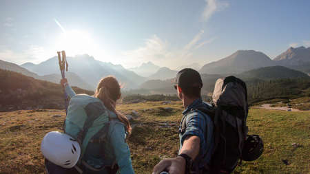 A couple enjoying an early morning in Italian Dolomites. The valley below is shrouded in morning haze. In the back there are high mountain chains. Sun slowly rising above the peaks. Golden hour.の写真素材