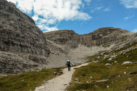 A woman hiking in a high and desolated mountains in Italian Dolomites. The lower parts of the mountains are overgrown with moss and grass. Raw and unspoiled landscape. Clear and sunny day. Solitudeの写真素材