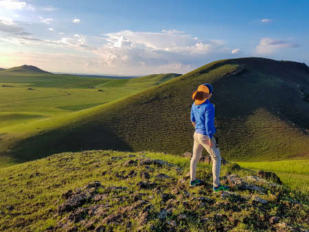A man standing on a green hill in Xilinhot, Inner Mongolia and enjoys a sunset. He is wearing a...